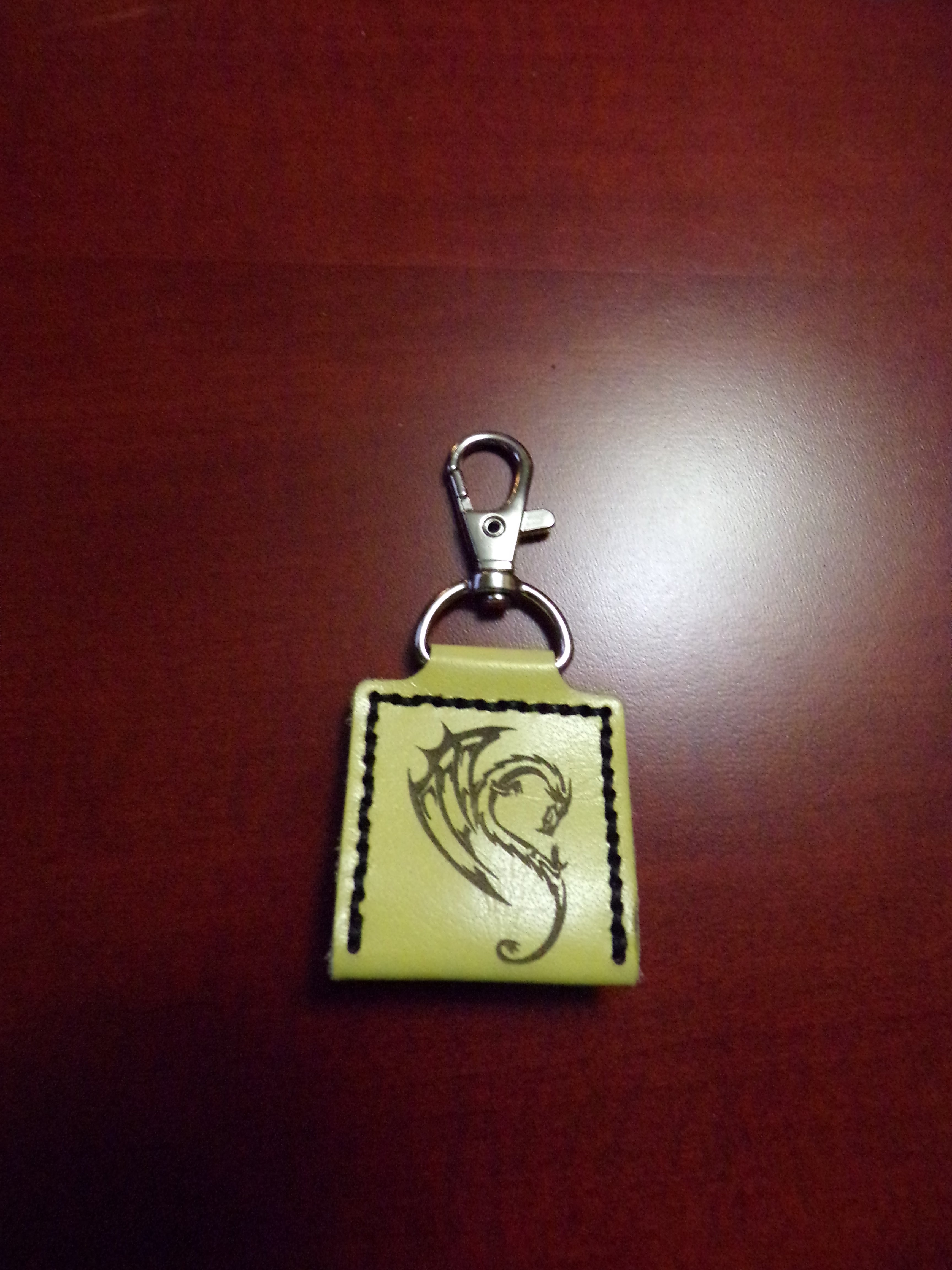 A green leather keychain with a square closure and a butterfly engraving, equipped with a metal clip.